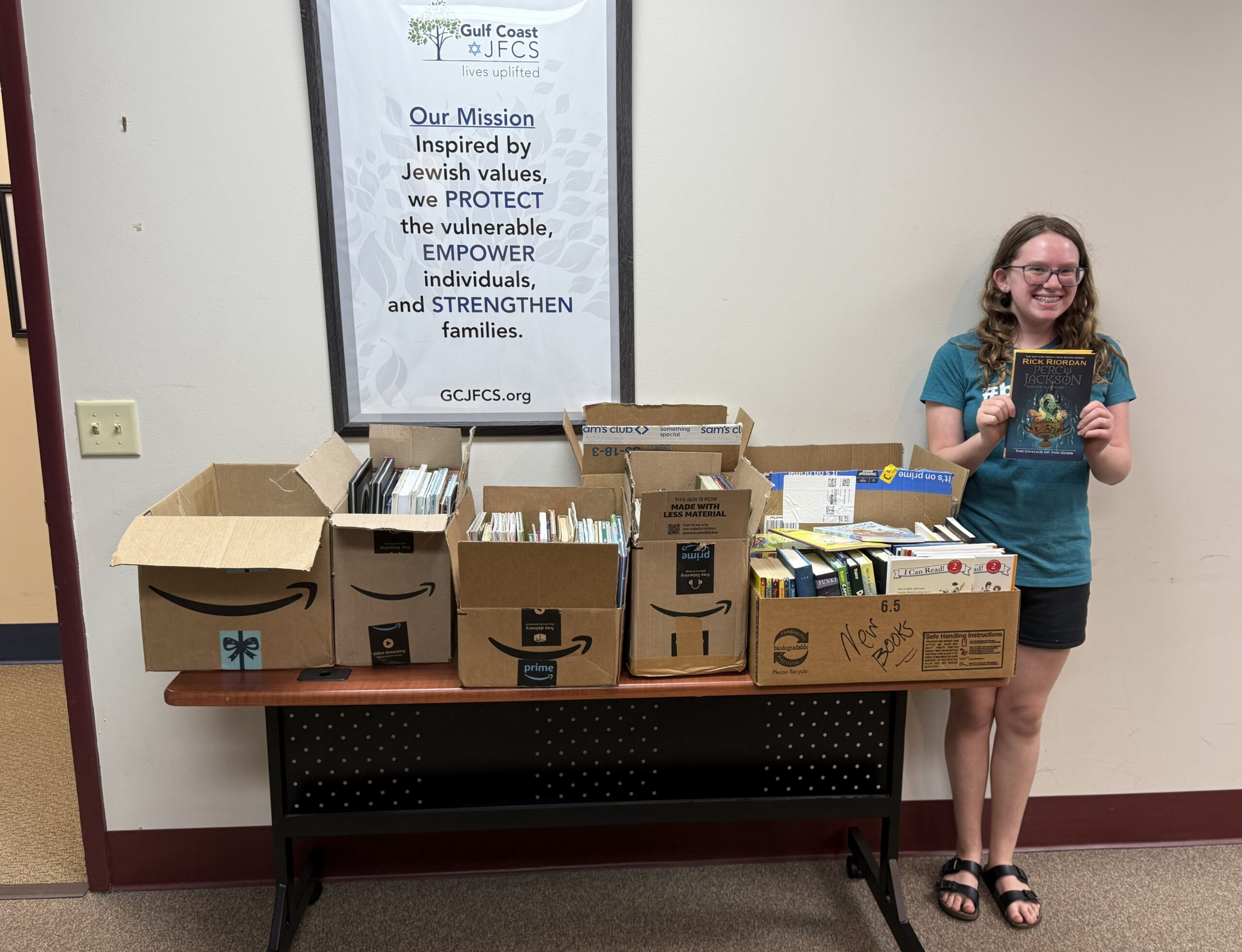 Girl stands next to table holding book. The table is full of boxes of books